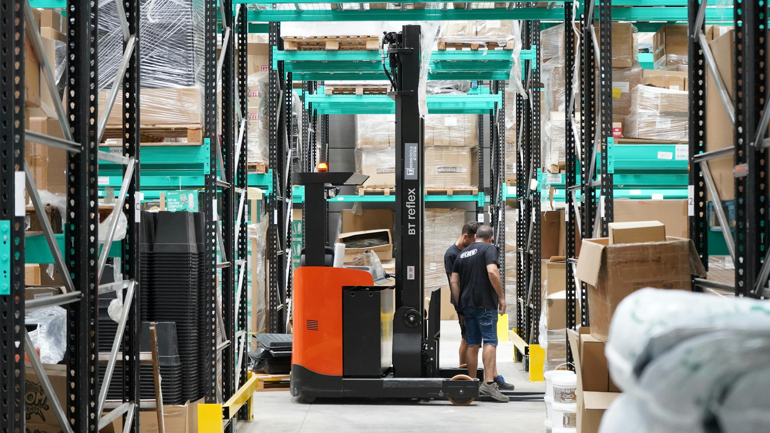 Warehouse scene featuring workers and a forklift navigating aisles for logistics and inventory management.
